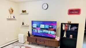 A living room with a flat-screen TV, wooden entertainment unit, bookshelves, decorative items, and a clock on the wall. - Getaway Spot Close to Red Rocks, Denver, Mtns (Lakewood)