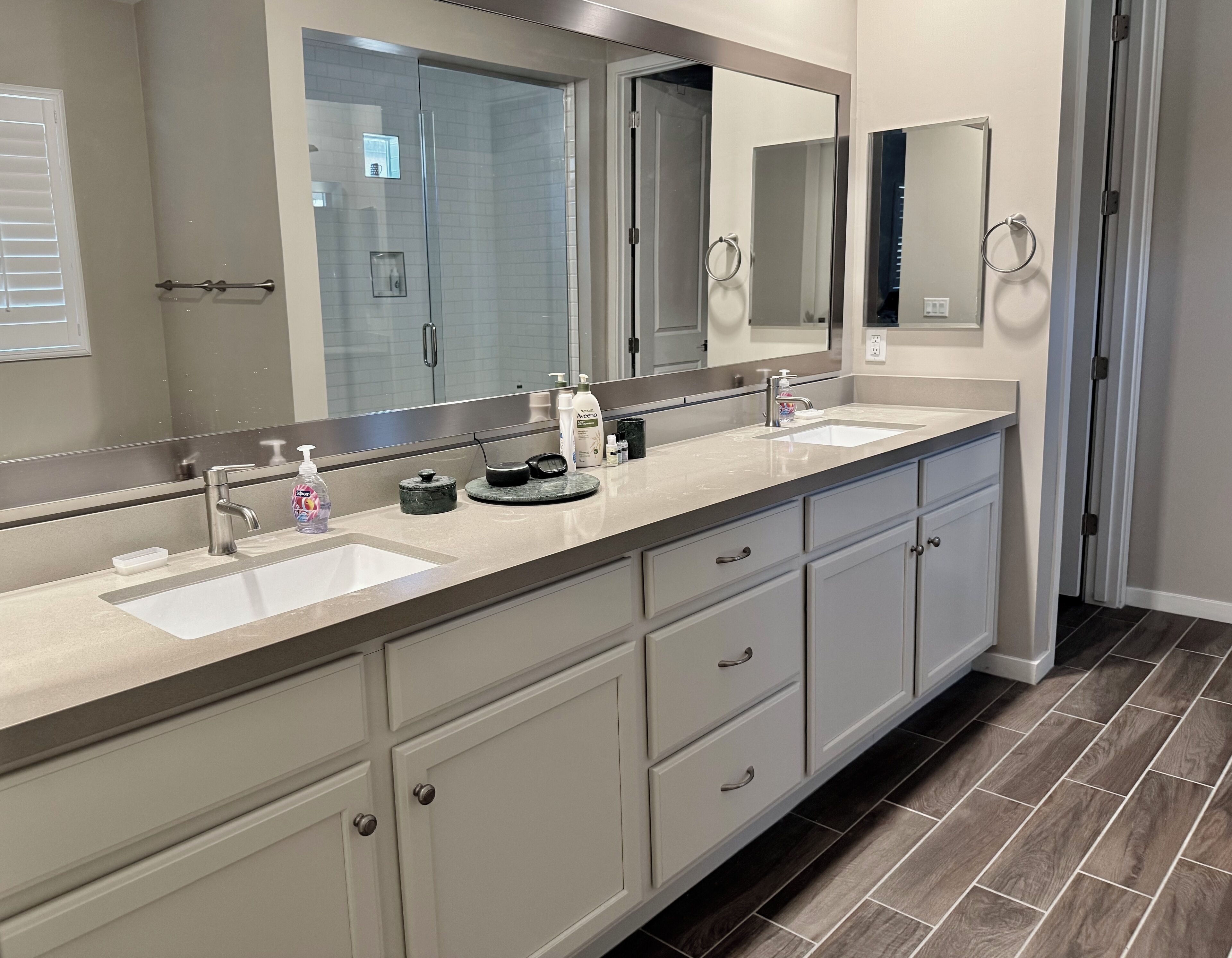 A modern bathroom with two sinks, a large mirror, and a shower area.
