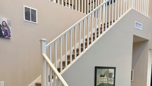 Un escalier dont les marches sont recouvertes de moquette et qui possède des rampes blanches, menant à l’étage supérieur.