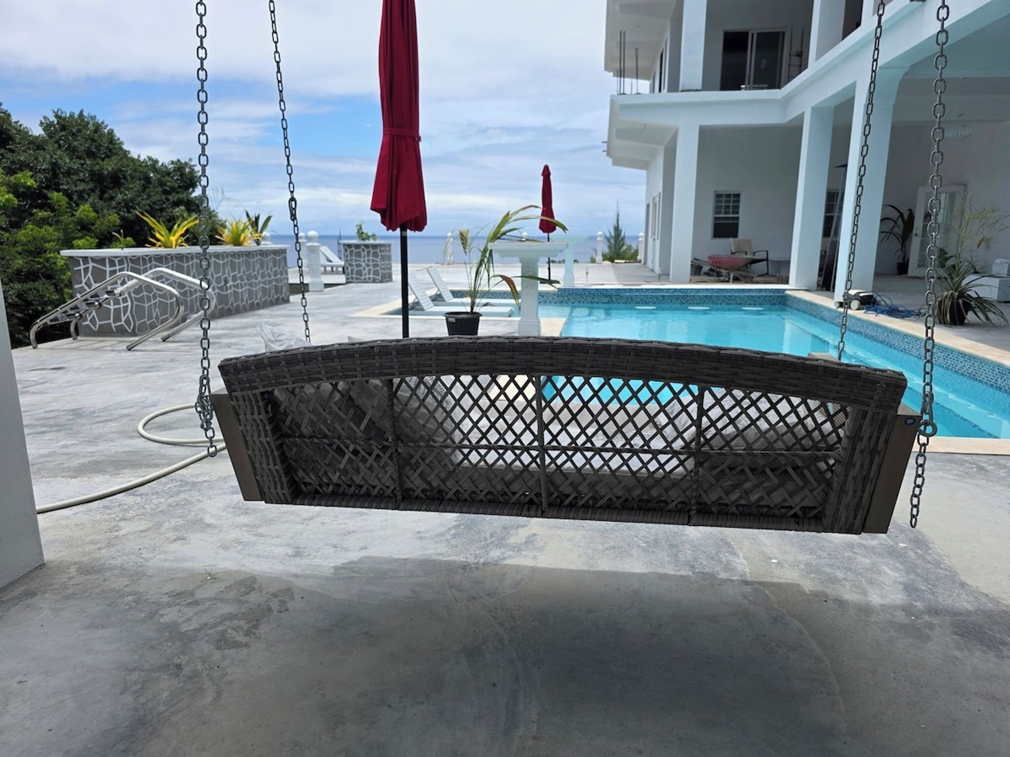 Un fauteuil suspendu en osier offrant une vue sur une piscine et un bâtiment en arrière-plan.