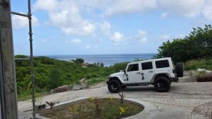 A white off-road vehicle parked on a paved area with a view of the ocean and greenery in the background.