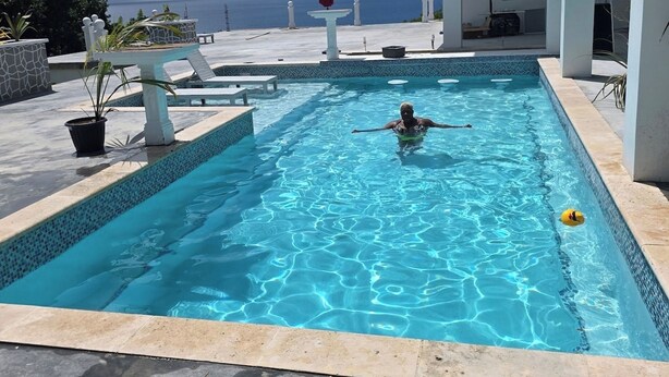 A swimming pool with a view of the ocean, surrounded by a white building with columns.