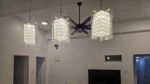 A modern living room with a flat-screen TV, a ceiling fan, and three pendant lights.