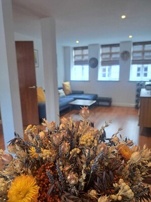 Un salon avec un canapé, une table basse et une composition décorative de fleurs séchées au premier plan.