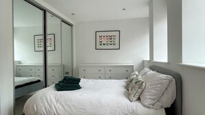 Un dormitorio con cama, cómoda, espejo y una obra de arte enmarcada en la pared.
