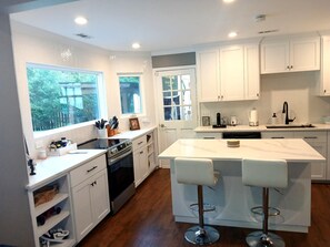 A modern kitchen with white cabinets, a central island with bar stools, a built-in oven, and a large window providing natural light. - South Charlotte 3BR w/ Pool, Fenced in and Pet-Friendly - Near Ballantyne! (Charlotte)