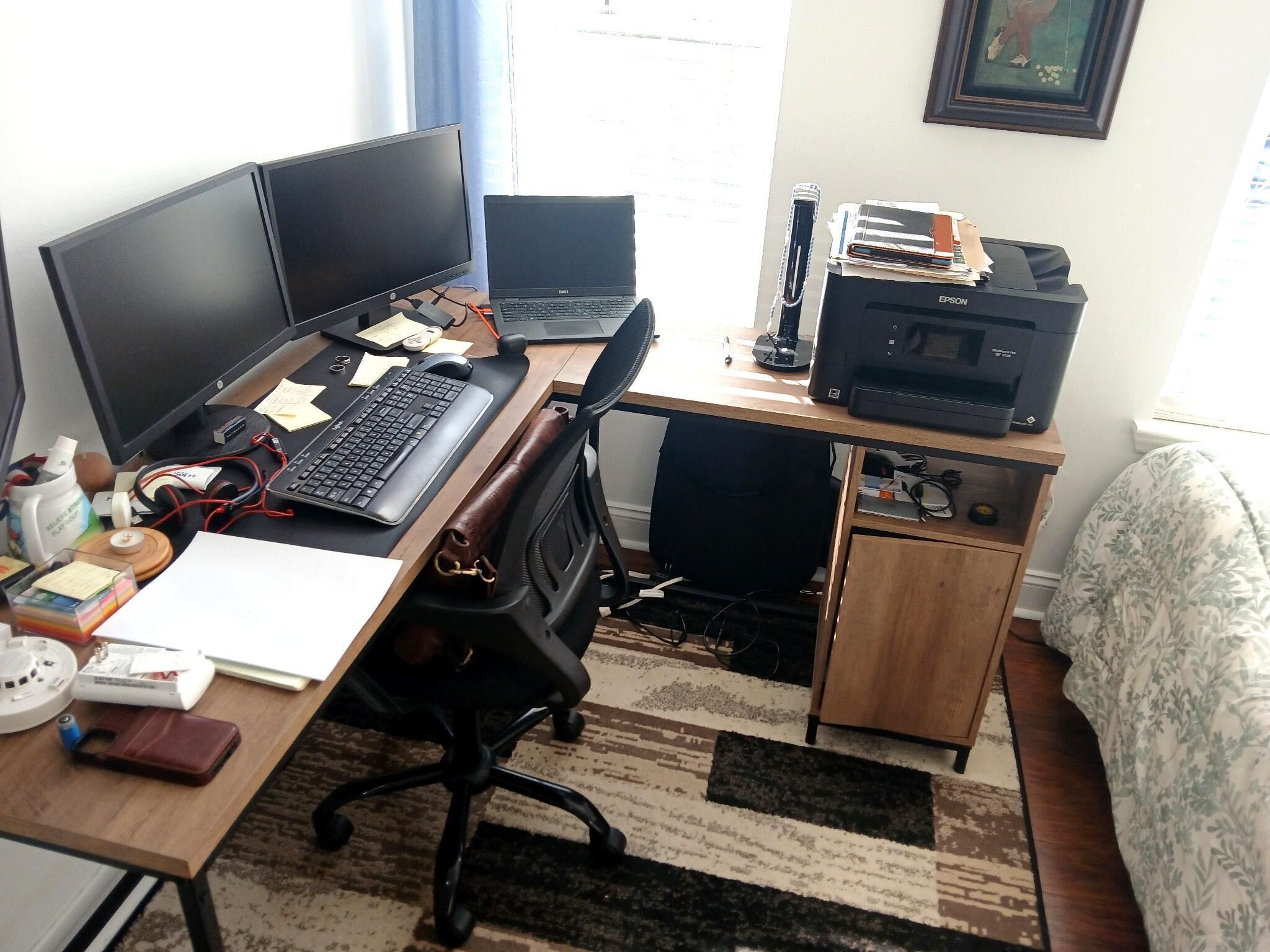 A home office with two monitors, a laptop, a printer, and various office supplies on a desk.