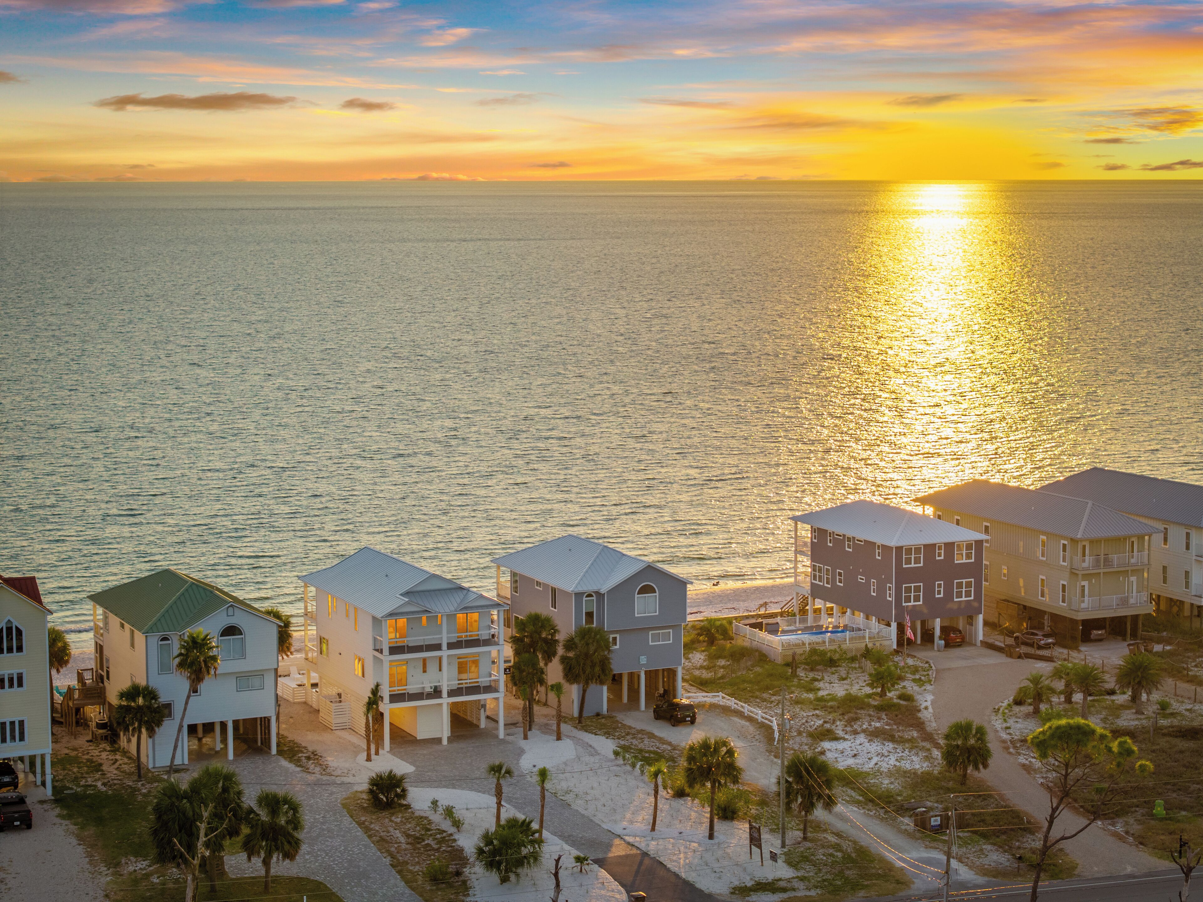 Un hôtel en bord de mer, composé de plusieurs bâtiments, avec une plage et une vue sur le coucher de soleil sur l’océan.