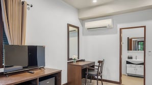 A hotel room with a TV, desk, chair, and a bathroom with a sink and mirror.