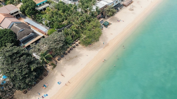 An aerial view of a beach with clear turquoise water, a sandy shore, and several beach umbrellas.