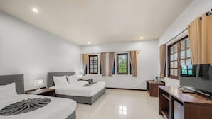 A hotel room with two beds, a TV, a desk, and a window with curtains.