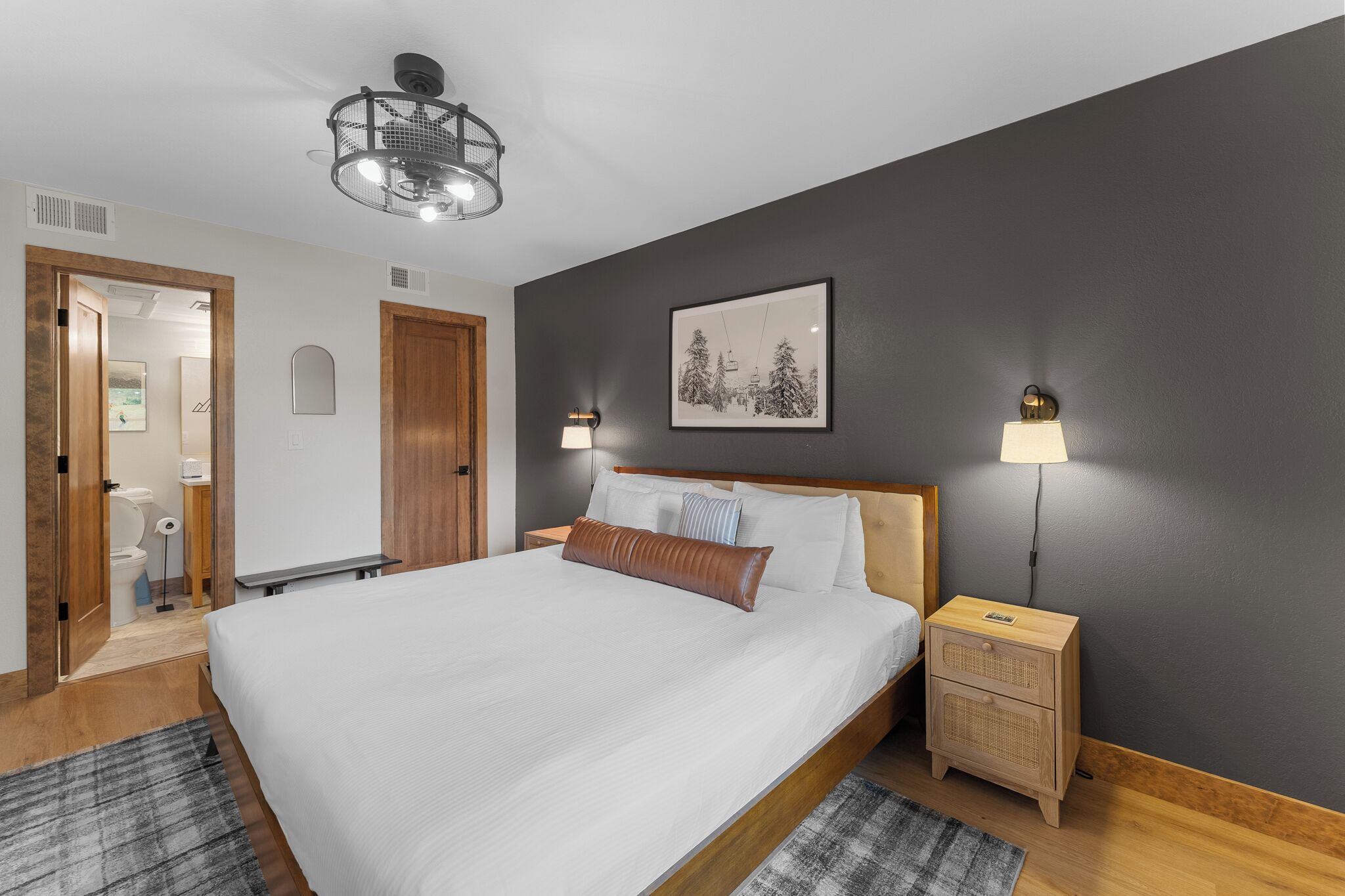 Un dormitorio con una cama grande, dos lámparas de noche, una luz de techo, un cuadro en la pared y una mesita de noche de madera.