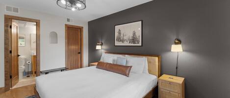 Un dormitorio con una cama grande, dos lámparas de noche, una luz de techo, un cuadro en la pared y una mesita de noche de madera.