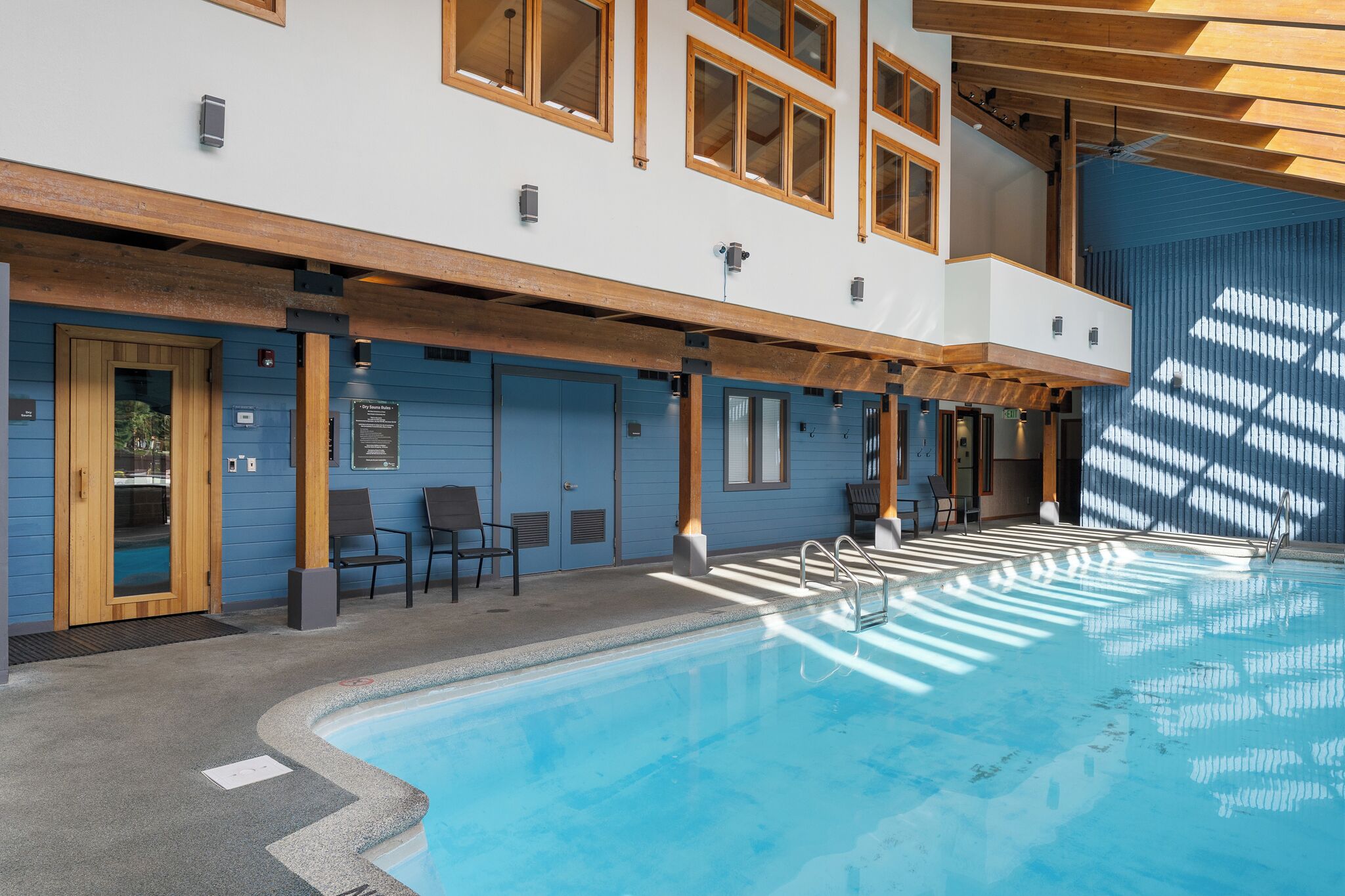 Une piscine intérieure moderne, avec une vue dégagée sur l’espace piscine, des poutres en bois et un mur extérieur bleu.