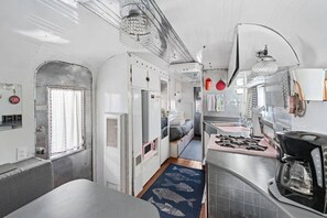 Un intĂ©rieur Ă©troit et fermĂ© comprenant un coin cuisine, un petit espace salon et une fenĂȘtre.