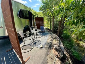 Un terrain de camping équipé d’une table et de chaises, d’un espace abrité et d’une caravane verte.