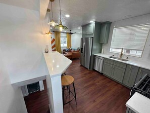 A modern kitchen with a central island, stainless steel appliances, and a dining area with a brown leather sofa.