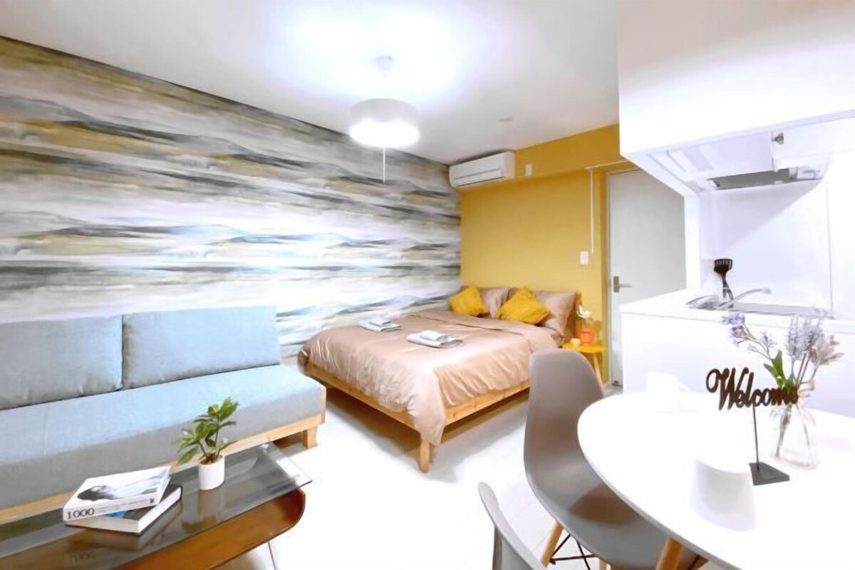 A modern bedroom with a bed, a sofa, a dining table, and a small kitchen area.