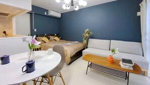 A modern room with a bed, a sofa, a round table with two mugs, and a ceiling light fixture. - Nestay apartment Tokyo Ginza (Tokyo)
