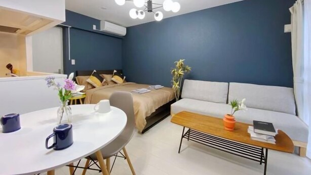 A modern room with a bed, a sofa, a round table with two mugs, and a ceiling light fixture. - Nestay apartment Tokyo Ginza (Tokyo)