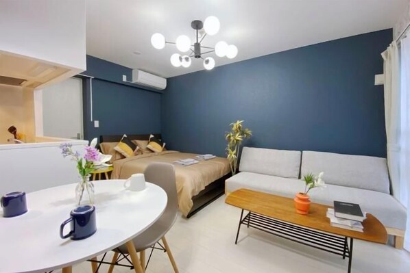 A modern room with a bed, a sofa, a round table with two mugs, and a ceiling light fixture. - Nestay apartment Tokyo Ginza (Tokyo)