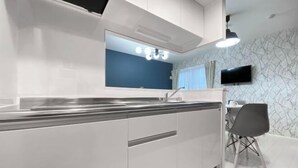A modern kitchen with white cabinets, a black countertop, a built-in sink, and a wall-mounted TV. - Nestay apartment Tokyo Ginza (Tokyo)
