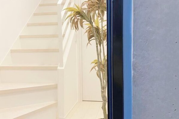 A staircase with white steps leading upwards, a blue-framed window, and a potted plant to the right. - Nestay apartment Tokyo Ginza (Tokyo)