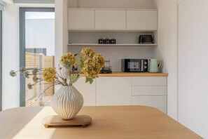A kitchen with a wooden table, a white vase with flowers, a microwave, and a coffee maker on the countertop.