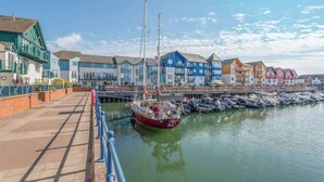 Un paseo marítimo con una hilera de edificios coloridos, un muelle con barcos y un cielo despejado.