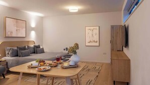 Una habitación de hotel moderna con una cama, una mesa de comedor con aperitivos, un florero con flores y un televisor de pantalla plana montado en la pared.