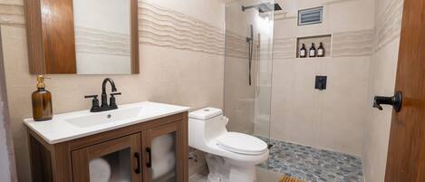 Un baño moderno con ducha envuelta en vidrio, un lavamanos blanco con mueble de madera y un inodoro.