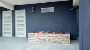 A modern building exterior with two white garage doors, a stone planter with colorful plants, and a small vent on the wall.