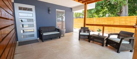 An outdoor patio with a wooden ceiling, a grey sofa, wicker chairs, and a small table.