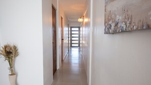 A hallway with a wooden door, a vase with dried flowers, and a painting on the wall.