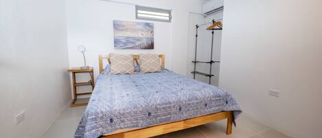Un dormitorio con cama de madera, mesita de noche, lámpara colgante, aire acondicionado instalado en la pared y ventana con vista al cielo.