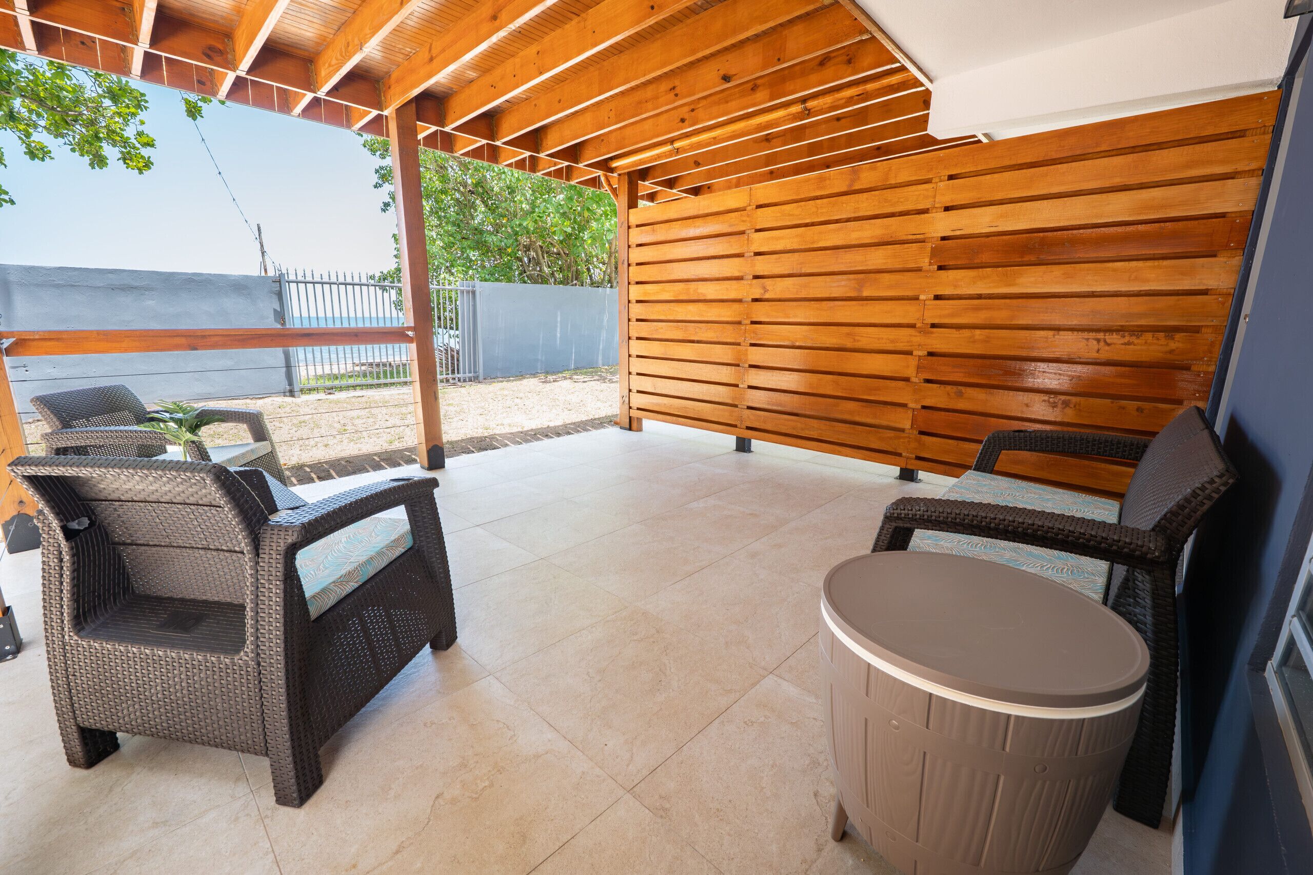 Un patio al aire libre con mobiliario de mimbre, una mesa redonda y una estructura de techo de madera.