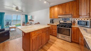Une cuisine spacieuse avec des meubles en bois, un grand îlot central, des appareils électroménagers en acier inoxydable et une vue sur l’extérieur.