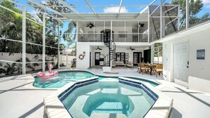 Ein Poolbereich mit zwei Whirlpools und einem Flamingo-Schwimmpunkt. Es gibt eine überdachte Terrasse mit Geländer und einer Treppe, die zu einer erhöhten Ebene führt.