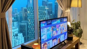 En tv-apparat som visar en mängd olika kanaler och har en utsikt över stadsbilden genom stora fönster.