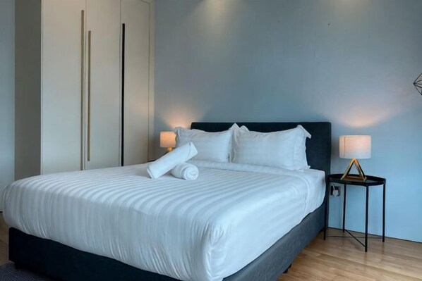 A neatly made bed with white linens, a dark headboard, and two bedside lamps on a nightstand.
