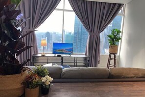 A living room with a sofa, a television, and a window with curtains. - Stella @ Vortex Suites KLCC (Kuala Lumpur)