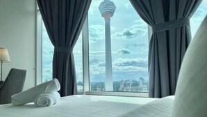 Ett hotellrum med en säng, en hoprullad handduk och utsikt över ett torn genom stora fönster.