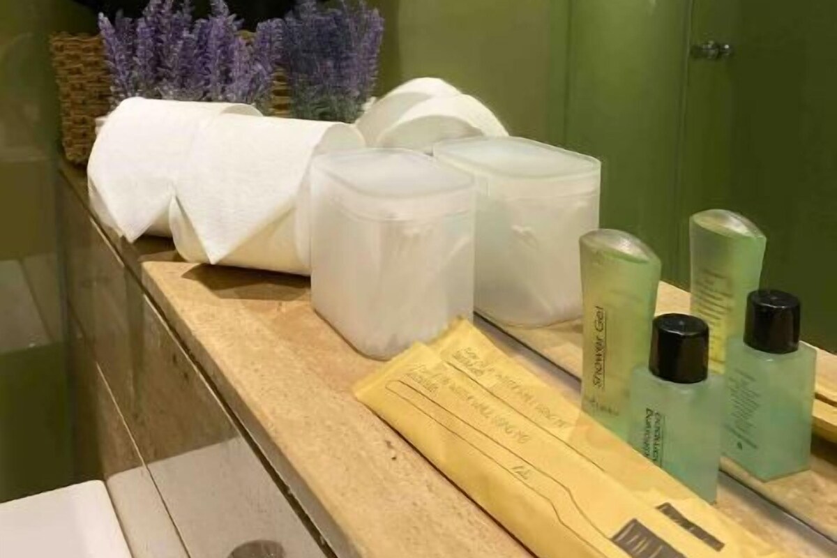 Un baño con pared verde, una planta en maceta, una toalla, un recipiente blanco y artículos de aseo.