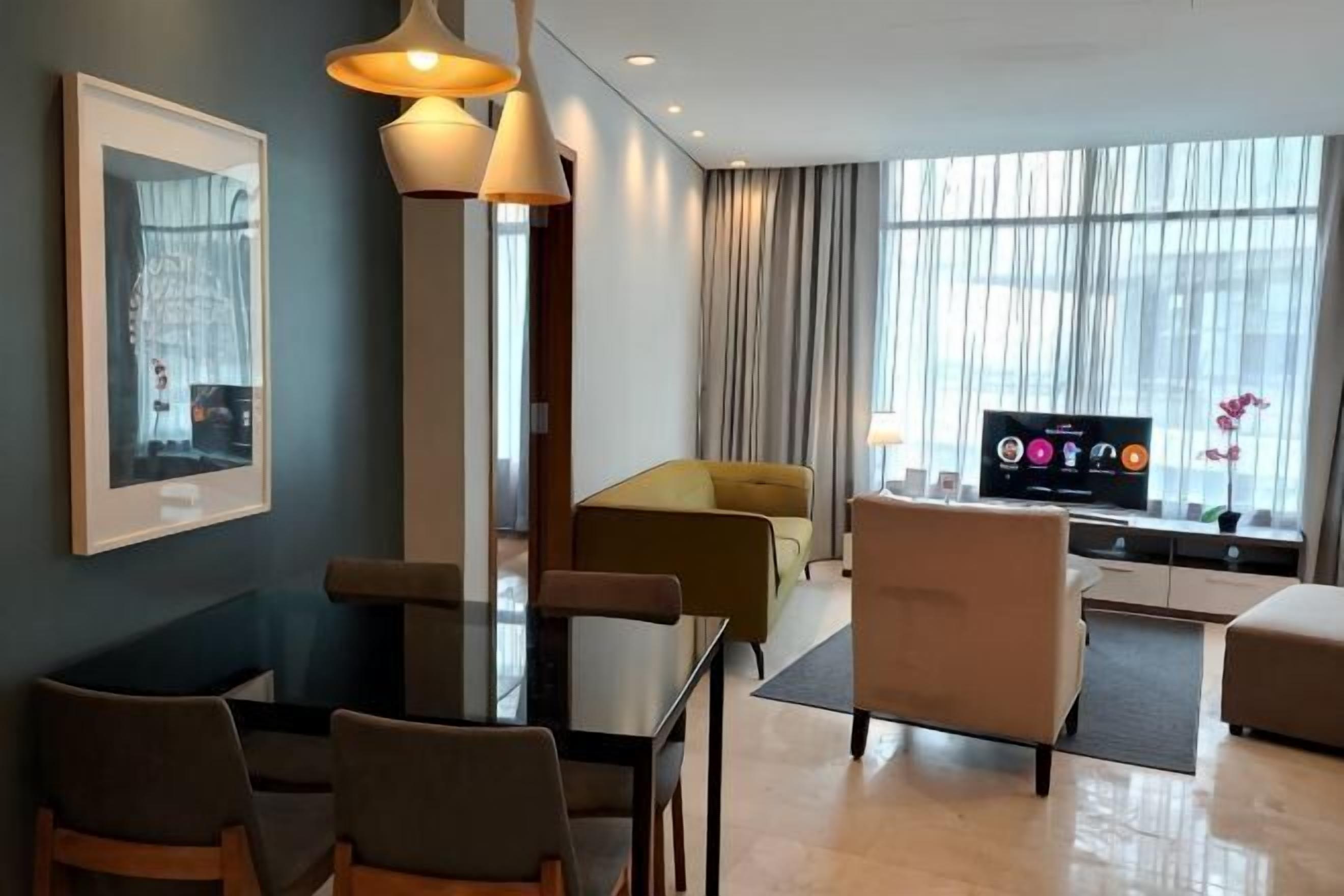A modern hotel room with a dining table, chairs, a sofa, a TV, and large windows.