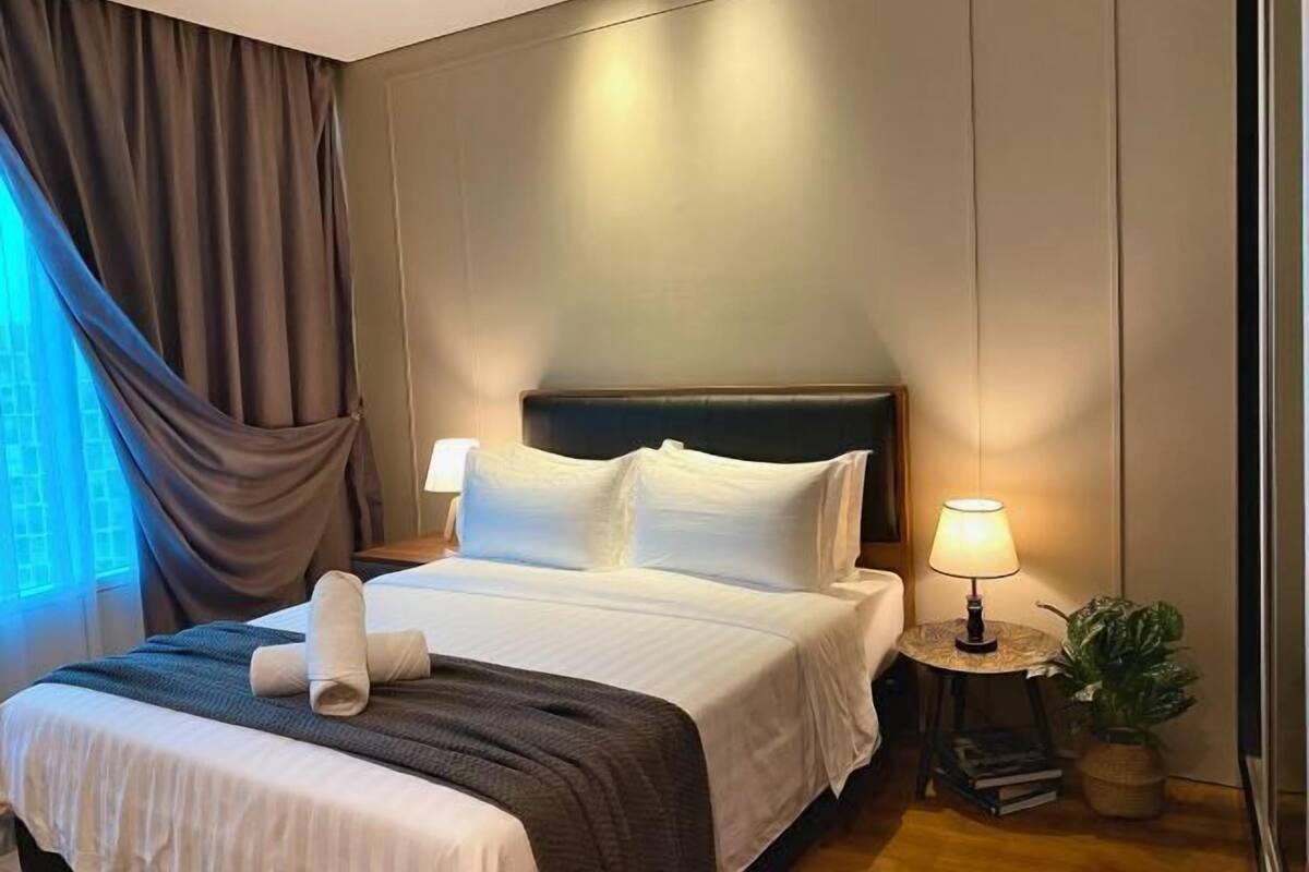 A hotel room with a bed, curtains, a nightstand with a lamp, and a small plant.
