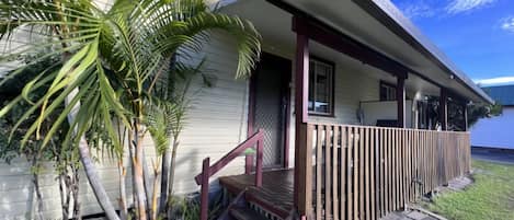 Una casa con un porche de madera, una pequeña escalera y una palmera.