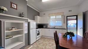 Eine kompakte Küche mit weißen Schränken, einem Kühlschrank, einem Backofen und einem Esstisch mit Stühlen.