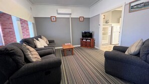 A living room with two sofas, a coffee table, a TV, and a bookshelf. - Cottage 1 ~ Come and relax by the river! (Sussex Inlet)