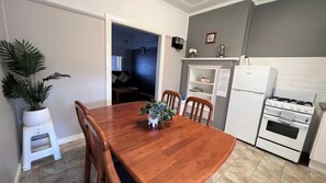 A compact kitchen with a wooden dining table, white cabinets, and a white refrigerator. - Cottage 1 ~ Come and relax by the river! (Sussex Inlet)