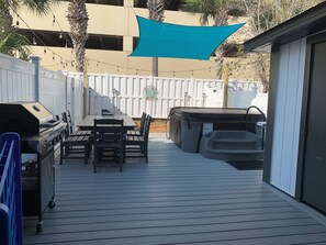 Een terras met een barbecue, een tafel, stoelen en een jacuzzi.